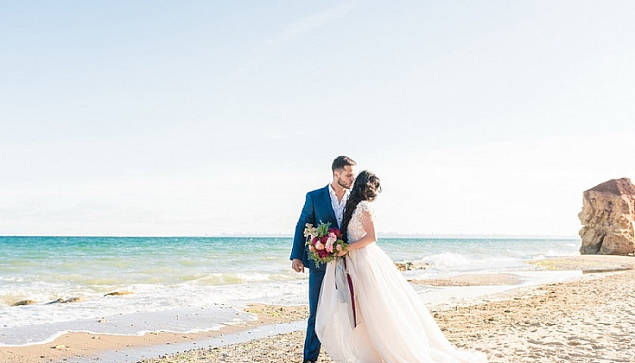  newlyweds holding hands and kissing near the beach