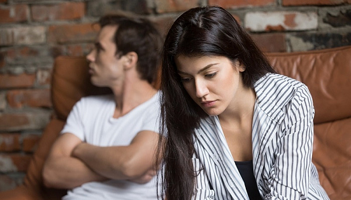 woman thinking of relationships problems sitting on sofa with offended husband